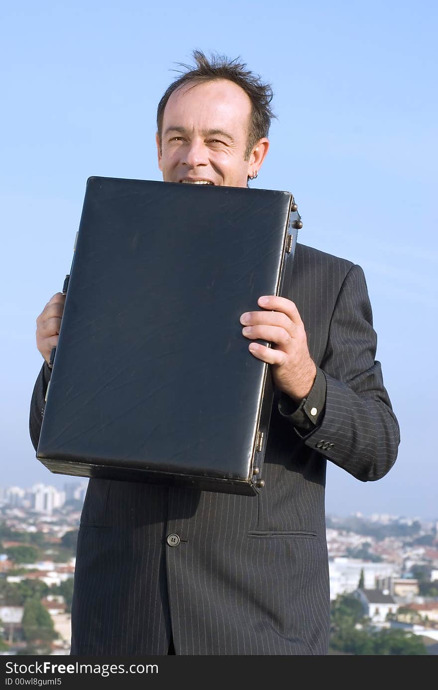 Latin american businessman standing on a city rooftop eating his briefcase in frustration. Latin american businessman standing on a city rooftop eating his briefcase in frustration