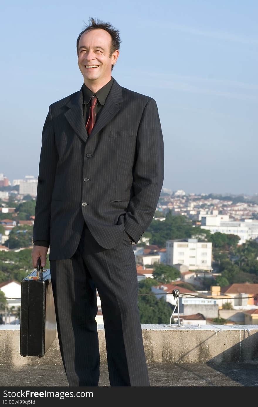 Businessman standing on a city rooftop and smiling while holding his briefcase. Businessman standing on a city rooftop and smiling while holding his briefcase