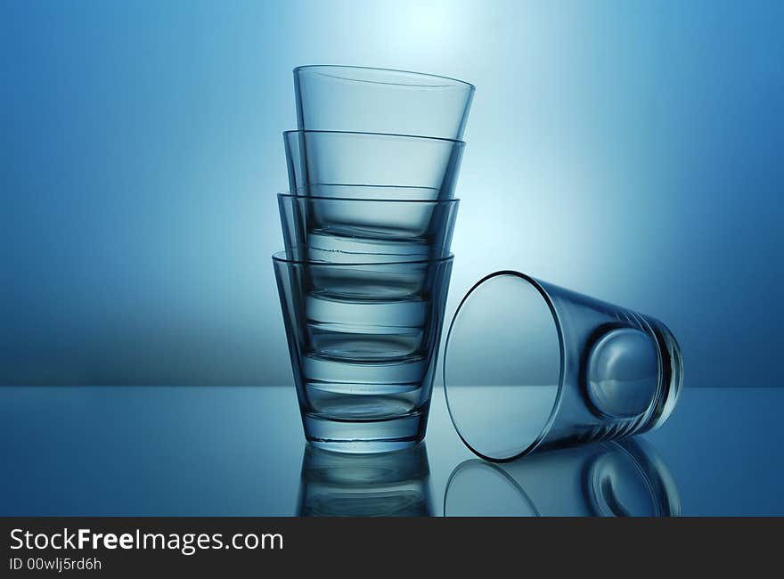 One and stack of empty shots for tequila or juice on blue background. One and stack of empty shots for tequila or juice on blue background