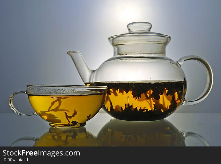 Glass teapot and cup with green tea on grey background. Glass teapot and cup with green tea on grey background