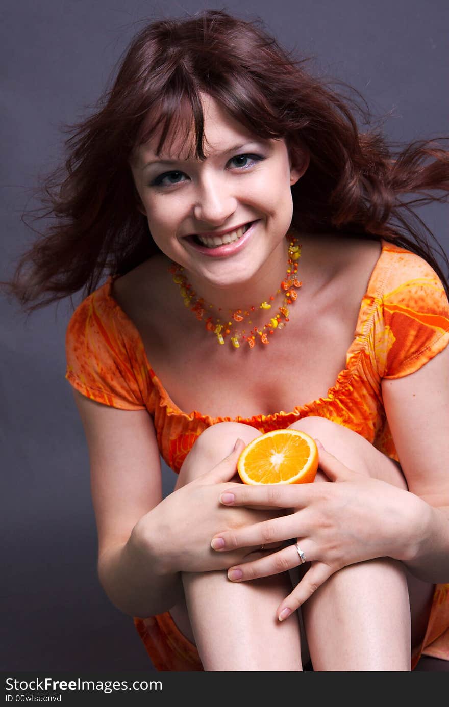 The positive smiling girl with an orange in hands. The positive smiling girl with an orange in hands