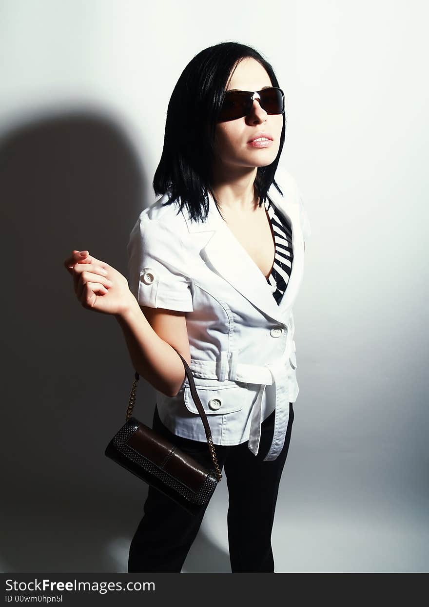 A high-key portrait about an attractive trendy lady with black hair who has a glamorous look. She is wearing sunglasses, black pants, a white coat and a stylish handbag. A high-key portrait about an attractive trendy lady with black hair who has a glamorous look. She is wearing sunglasses, black pants, a white coat and a stylish handbag.