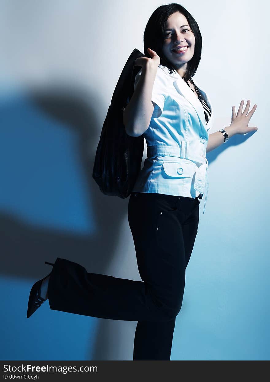 A high-key portrait about a cute stylish woman with black hair who is lighted with blue, she is lifting up her leg and she has an attractive look. She is wearing black pants, a white coat and a stylish handbag. A high-key portrait about a cute stylish woman with black hair who is lighted with blue, she is lifting up her leg and she has an attractive look. She is wearing black pants, a white coat and a stylish handbag.