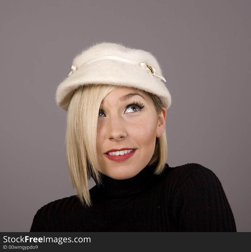 A blonde in a black turtleneck and a white fur hat looking up and to the left. A blonde in a black turtleneck and a white fur hat looking up and to the left.