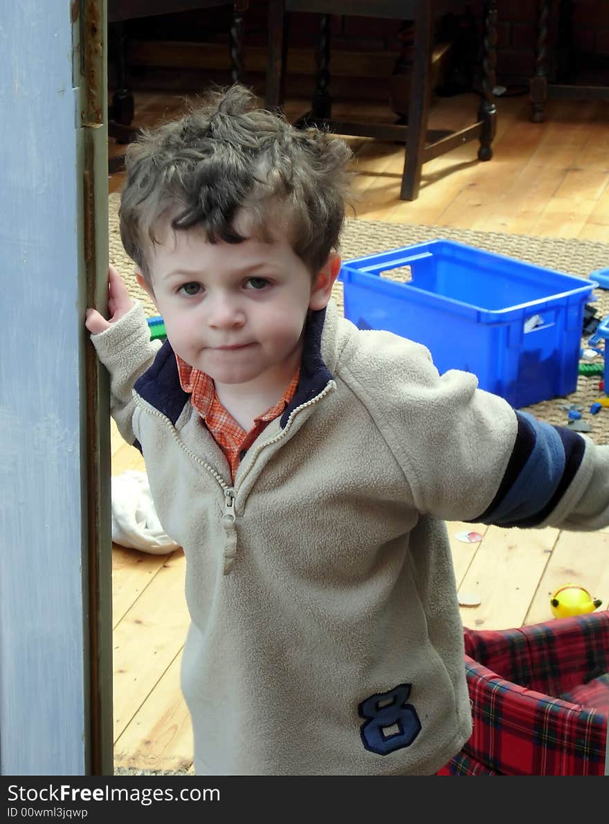 A thoughtful young child leans out of his playroom door. A thoughtful young child leans out of his playroom door.