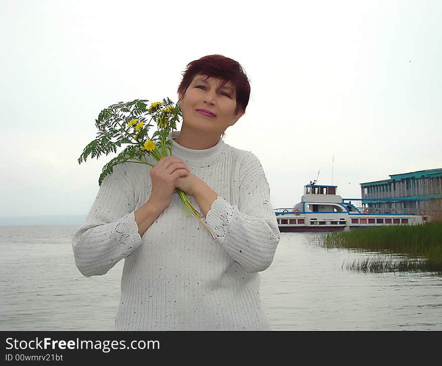 Trip to a province. Rural landscape. Happy business woman with the bouquet of the field flowers on a background of the river and excursion ship. Trip to a province. Rural landscape. Happy business woman with the bouquet of the field flowers on a background of the river and excursion ship.