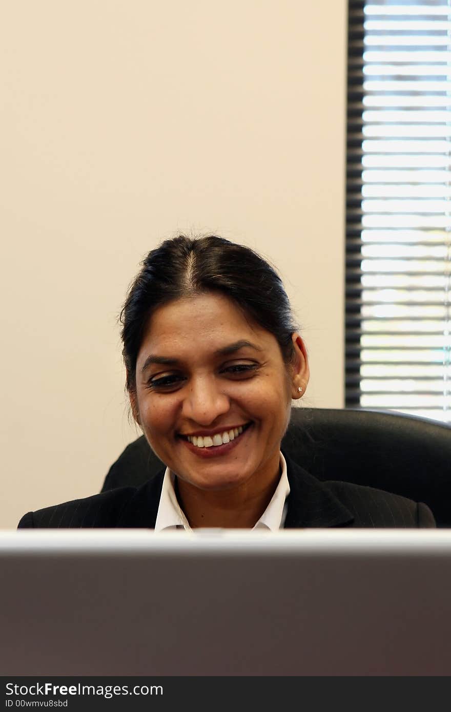 Indian businesswoman sitting behind her laptop with a huge smile on her face. Indian businesswoman sitting behind her laptop with a huge smile on her face