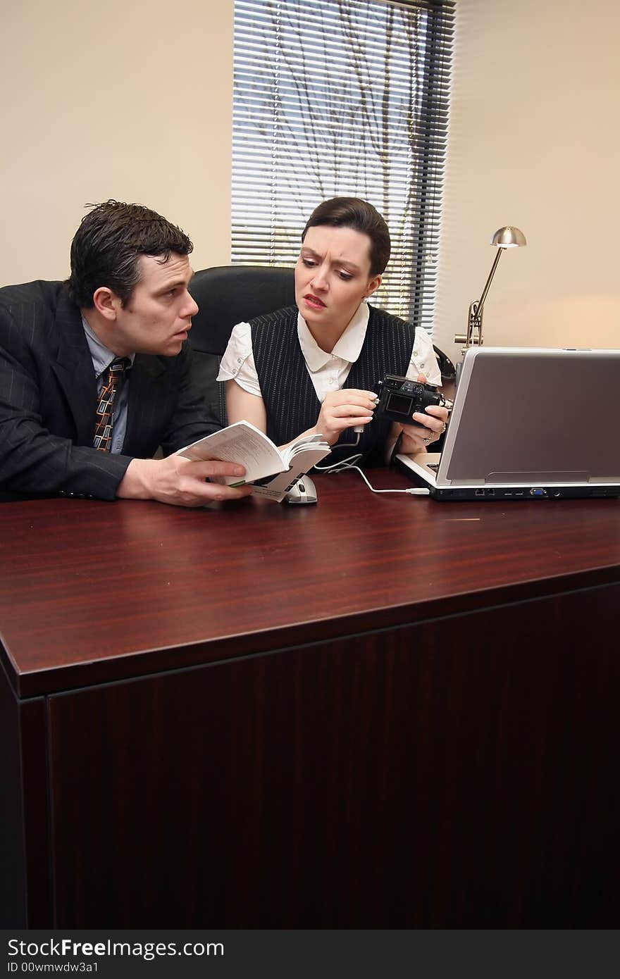 Male and female work colleagues trying to figure out how to connect a digital camera to a laptop. Male and female work colleagues trying to figure out how to connect a digital camera to a laptop