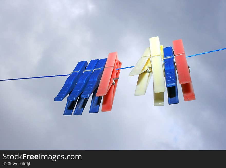 Colorful clothespins with rain drops on the rope on the sky background.