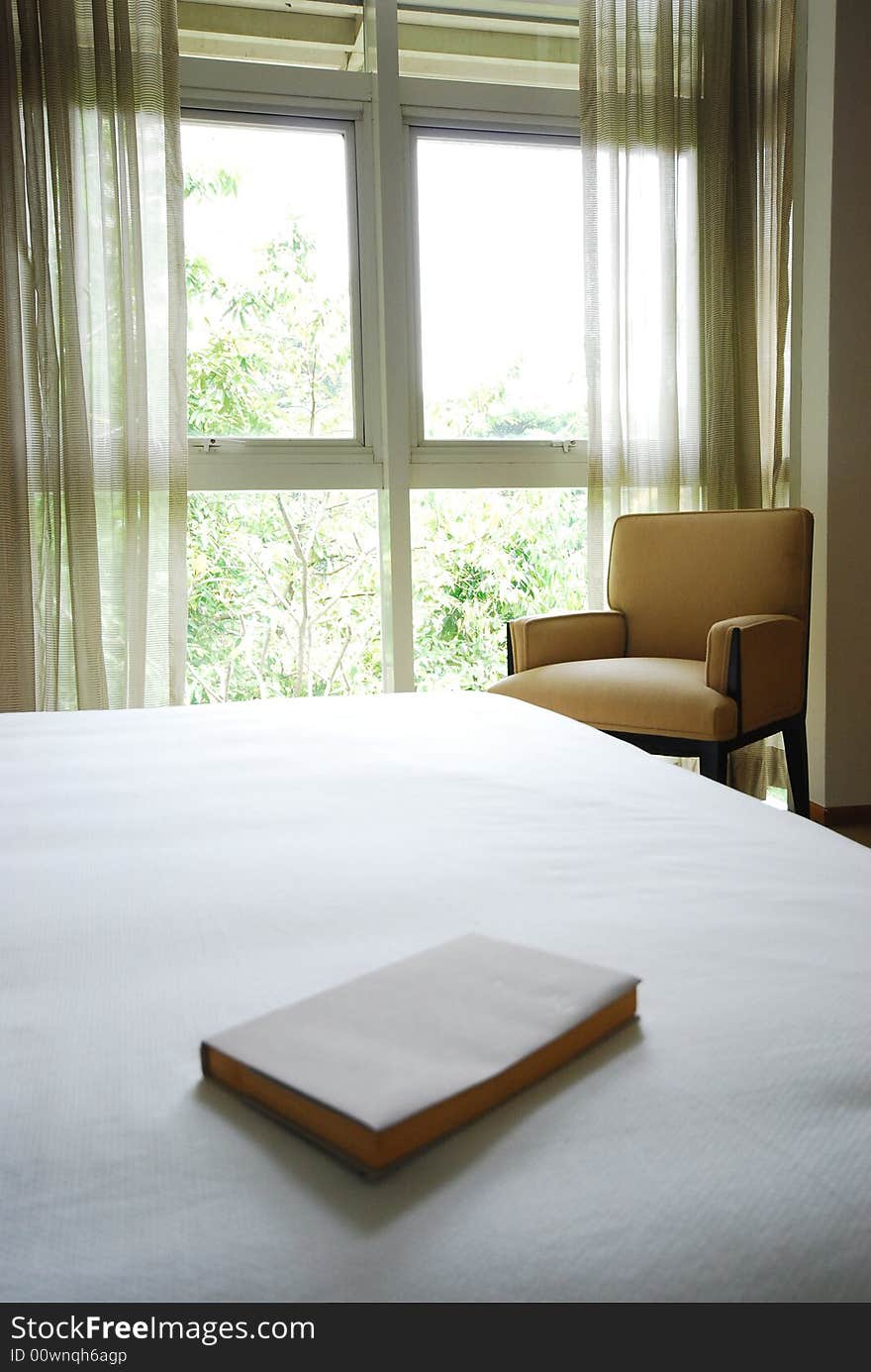 Book on the edge of a neatly made white bed. Book on the edge of a neatly made white bed.