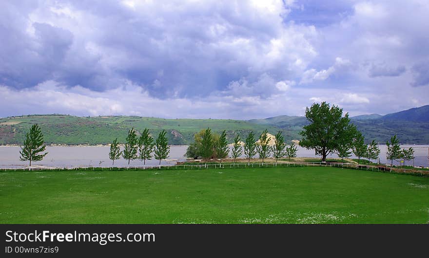 Various tree row by river under cloudy sky. Various tree row by river under cloudy sky