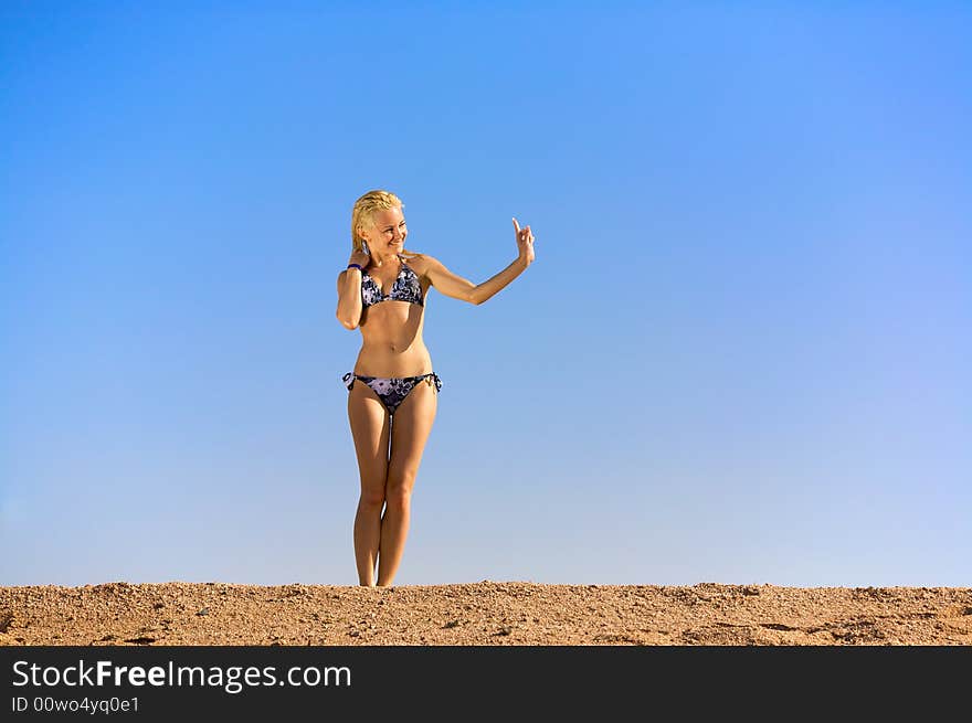 Young woman indicate direction with a finger. Blue sky on a background. Young woman indicate direction with a finger. Blue sky on a background