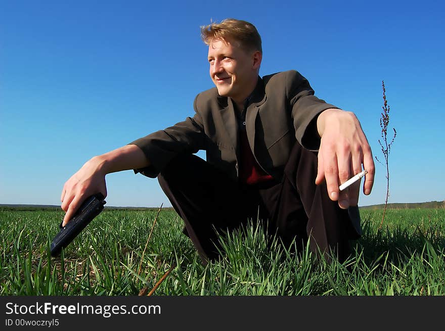 Young man squatting, with a gun and a cigarette, in a middle of a field. Young man squatting, with a gun and a cigarette, in a middle of a field