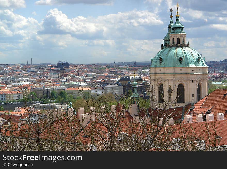 The Prague landscape with roofs of historical buildings. Top of an old cathedral at the right , tree branches б clouds and sky . The Prague landscape with roofs of historical buildings. Top of an old cathedral at the right , tree branches б clouds and sky .