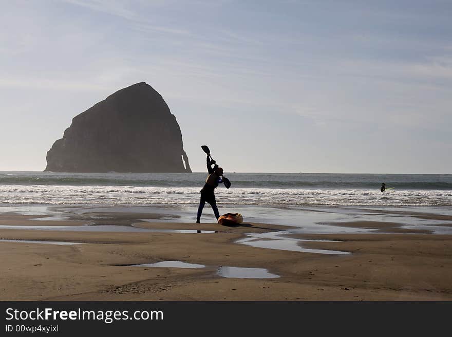 A silhouette of a kayaker getting ready to hit the waves on the beach.