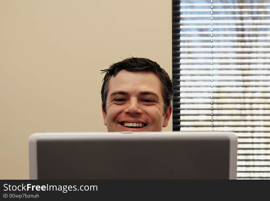 Businessman sitting behind a laptop screen with a broad smile on his face. Horizontally framed shot. Businessman sitting behind a laptop screen with a broad smile on his face. Horizontally framed shot