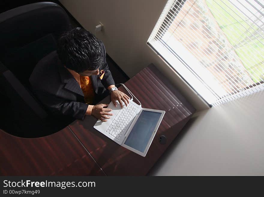 Overhead shot of a young businessman working on his laptop by a sunny window. Overhead shot of a young businessman working on his laptop by a sunny window