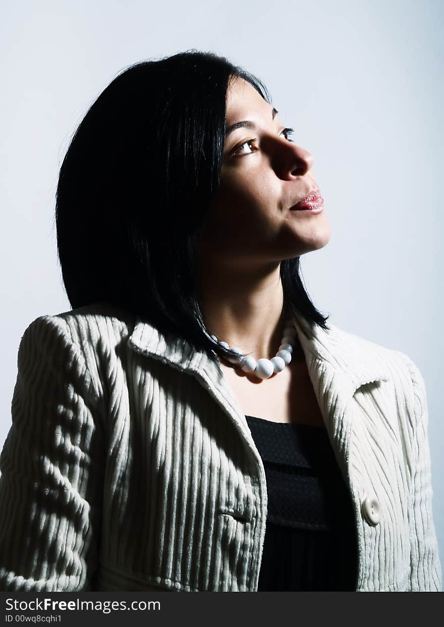 A high-key portrait about a young pretty woman with black hair who is looking up and she is dreaming. She is wearing a white coat, a black dress and a white necklace. A high-key portrait about a young pretty woman with black hair who is looking up and she is dreaming. She is wearing a white coat, a black dress and a white necklace.