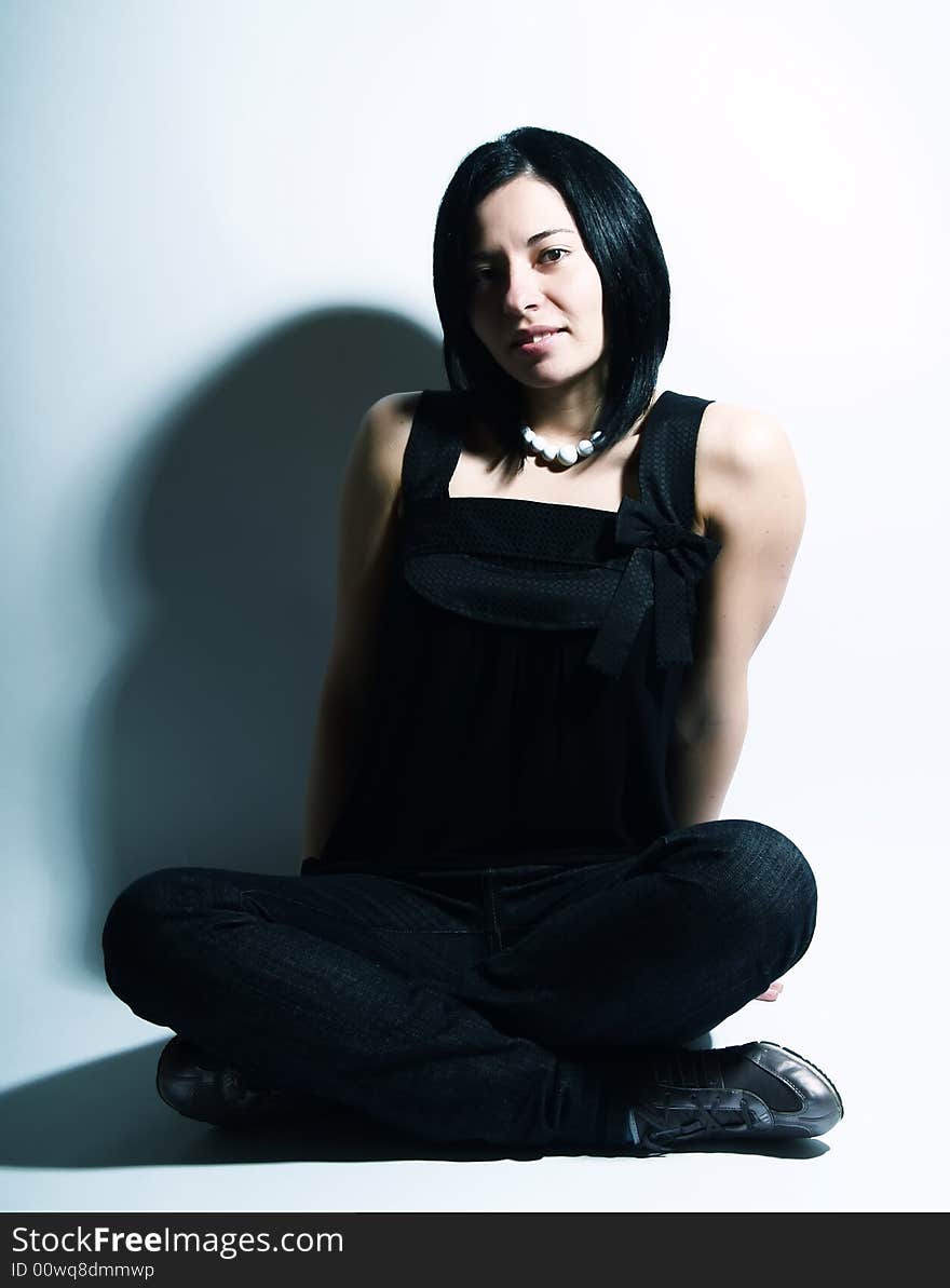 A portrait about an attractive trendy girl with black hair who is sitting and she has a charming look. She is wearing a black dress, blue jeans and a white necklace. A portrait about an attractive trendy girl with black hair who is sitting and she has a charming look. She is wearing a black dress, blue jeans and a white necklace.