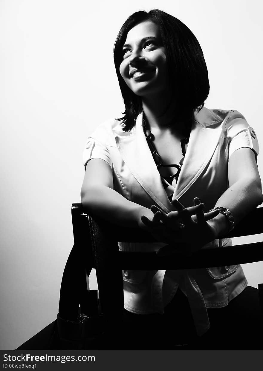 A black and white high-key portrait about a pretty trendy lady with black hair who is sitting on a chair, she is looking up and she is smiling. She is wearing a white coat and a stylish necklace. A black and white high-key portrait about a pretty trendy lady with black hair who is sitting on a chair, she is looking up and she is smiling. She is wearing a white coat and a stylish necklace.