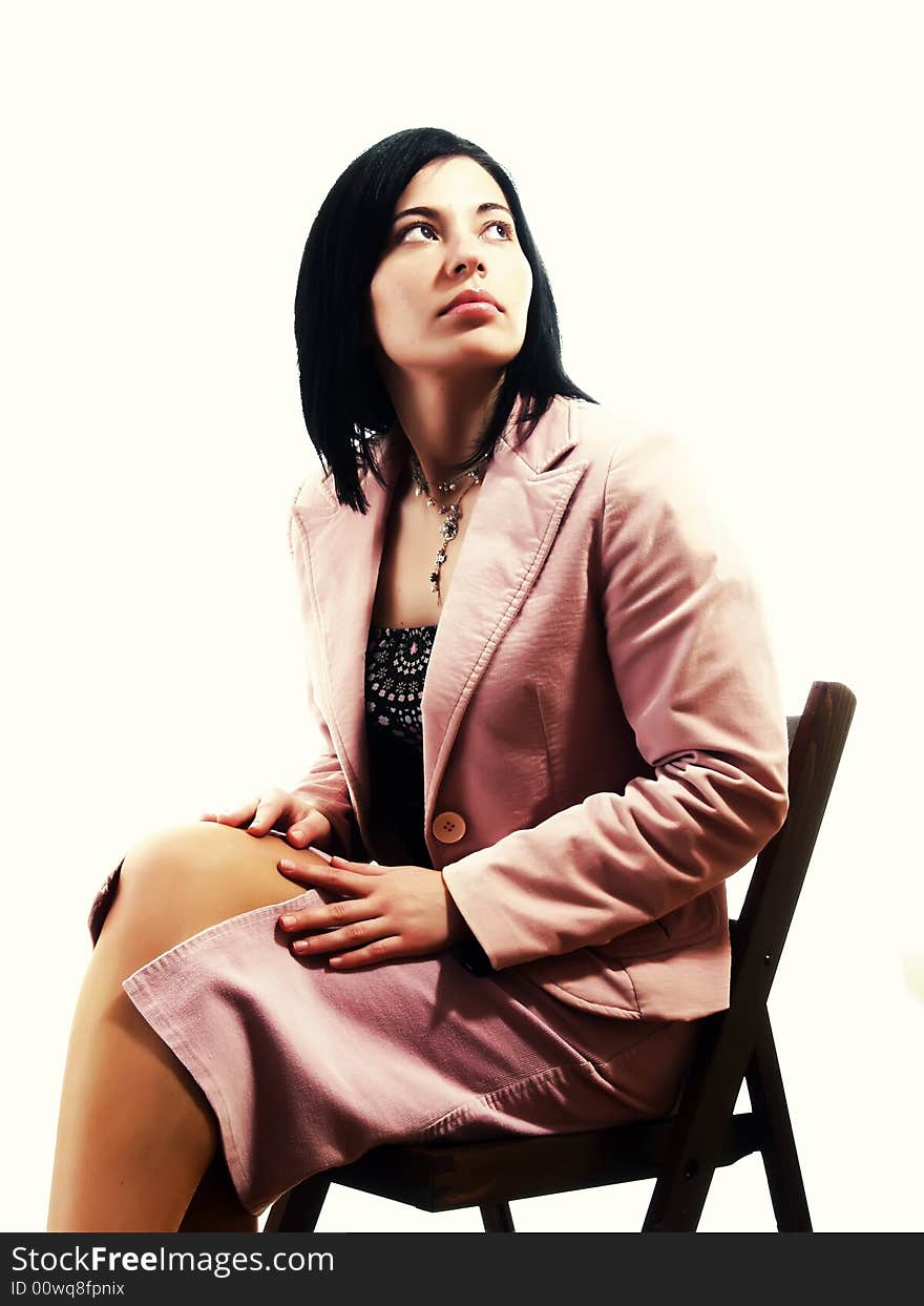 A portrait about an elegant trendy lady with black hair who is sitting on a chair and she is looking up. She is wearing a nice dress, a pink skirt and a pink stylish coat. A portrait about an elegant trendy lady with black hair who is sitting on a chair and she is looking up. She is wearing a nice dress, a pink skirt and a pink stylish coat.