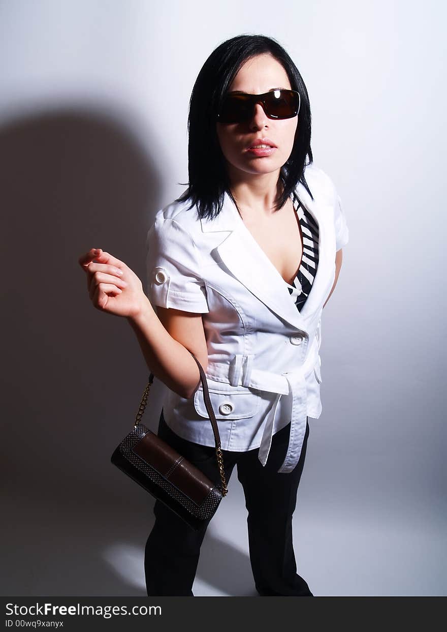 A high-key portrait about an attractive trendy lady with black hair who has a charming look. She is wearing sunglasses, black pants, a white coat and a stylish handbag. A high-key portrait about an attractive trendy lady with black hair who has a charming look. She is wearing sunglasses, black pants, a white coat and a stylish handbag.