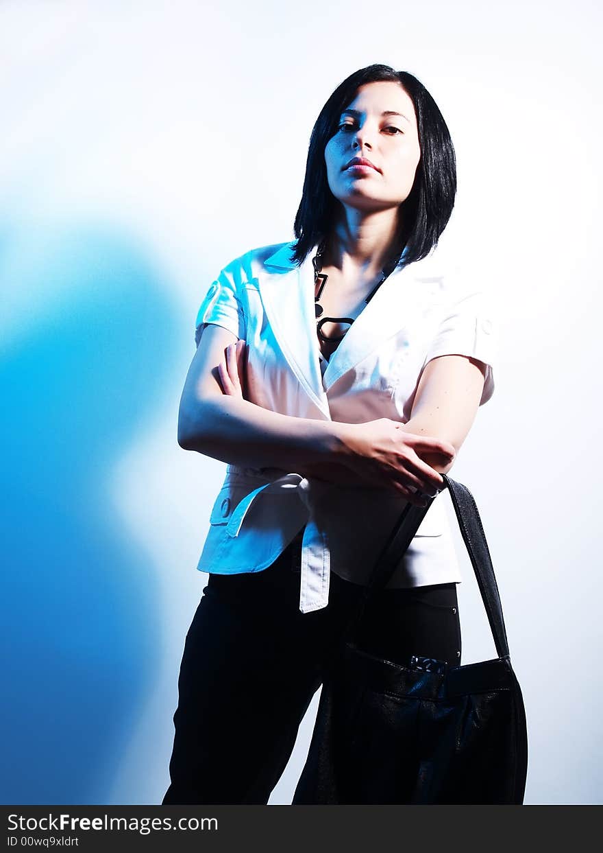 A high-key portrait about an attractive trendy lady with black hair who is lighted with blue and she has a charming look. She is wearing black pants, a white coat, a black necklace and a stylish handbag. A high-key portrait about an attractive trendy lady with black hair who is lighted with blue and she has a charming look. She is wearing black pants, a white coat, a black necklace and a stylish handbag.