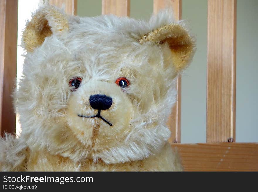 An antique well loved toy teddy bear sits in a wooden kitchen chair. An antique well loved toy teddy bear sits in a wooden kitchen chair.