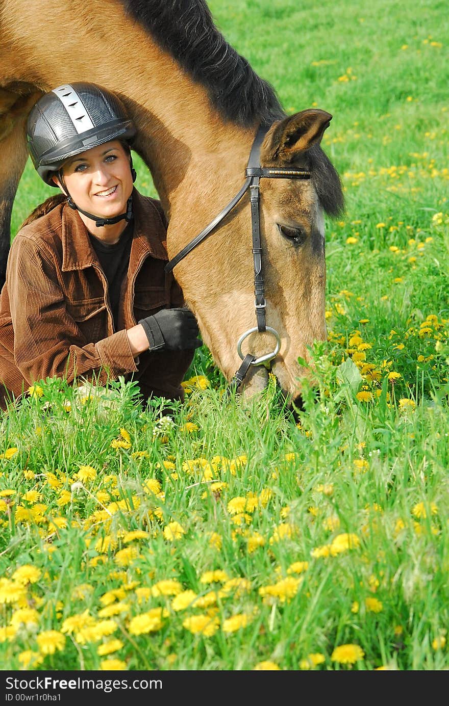 Woman kneeling in green field with yellow dandelions next to her horse. Woman kneeling in green field with yellow dandelions next to her horse.