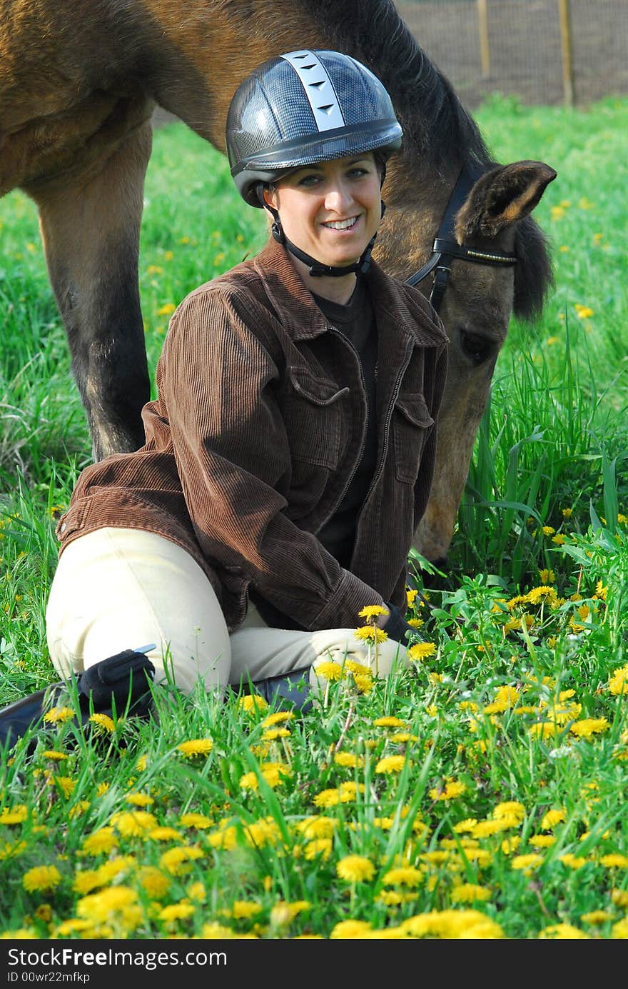 Woman sitting in green field with yellow dandelions next to her horse. Woman sitting in green field with yellow dandelions next to her horse.