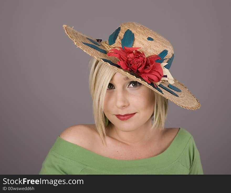 A blonde in green bouse with a flowered hat slanted and big eyes looking at the camera. A blonde in green bouse with a flowered hat slanted and big eyes looking at the camera