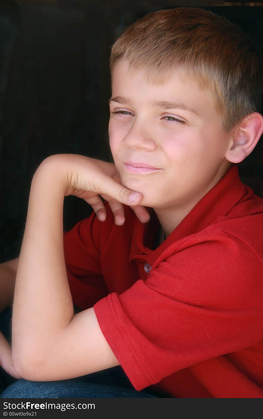 Cute boy in red shirt with hand on his chin, pleasant expression.