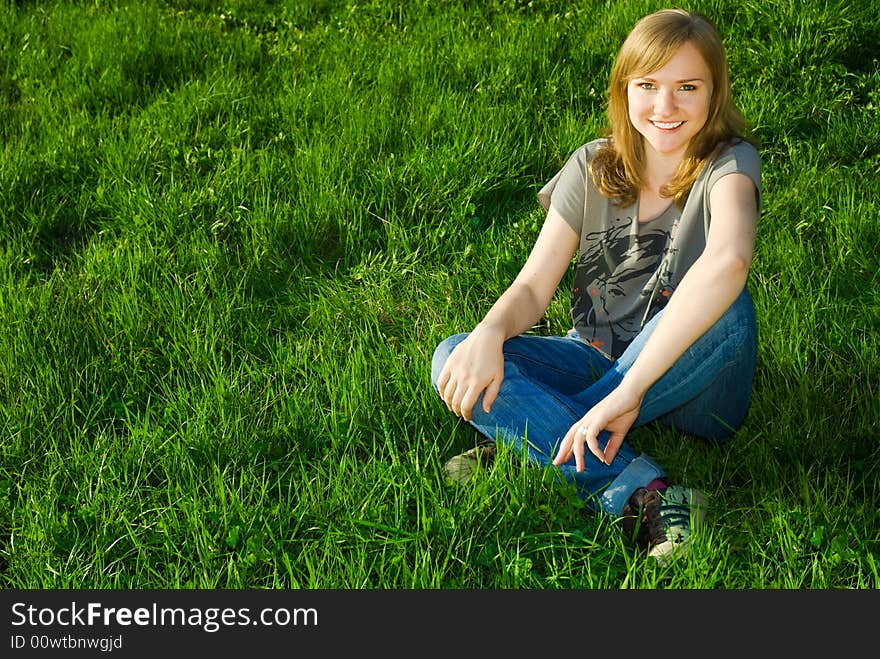 Beautiful and happy young woman with toothy smile, sitting on the grass, with copy space. Beautiful and happy young woman with toothy smile, sitting on the grass, with copy space