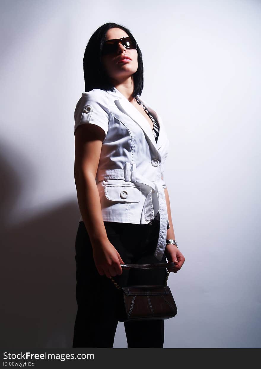 A high-key portrait about a pretty trendy lady with black hair who has an attractive look. She is wearing sunglasses, black pants, a white coat and a stylish purse. A high-key portrait about a pretty trendy lady with black hair who has an attractive look. She is wearing sunglasses, black pants, a white coat and a stylish purse.