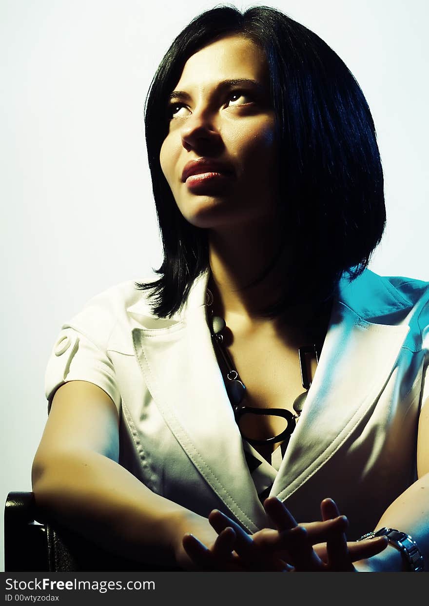 A high-key portrait about a cute trendy girl with black hair who is lighted in blue and yellow, she is sitting on a chair, she is looking up and she is dreaming something. She is wearing a white coat and a stylish necklace. A high-key portrait about a cute trendy girl with black hair who is lighted in blue and yellow, she is sitting on a chair, she is looking up and she is dreaming something. She is wearing a white coat and a stylish necklace.