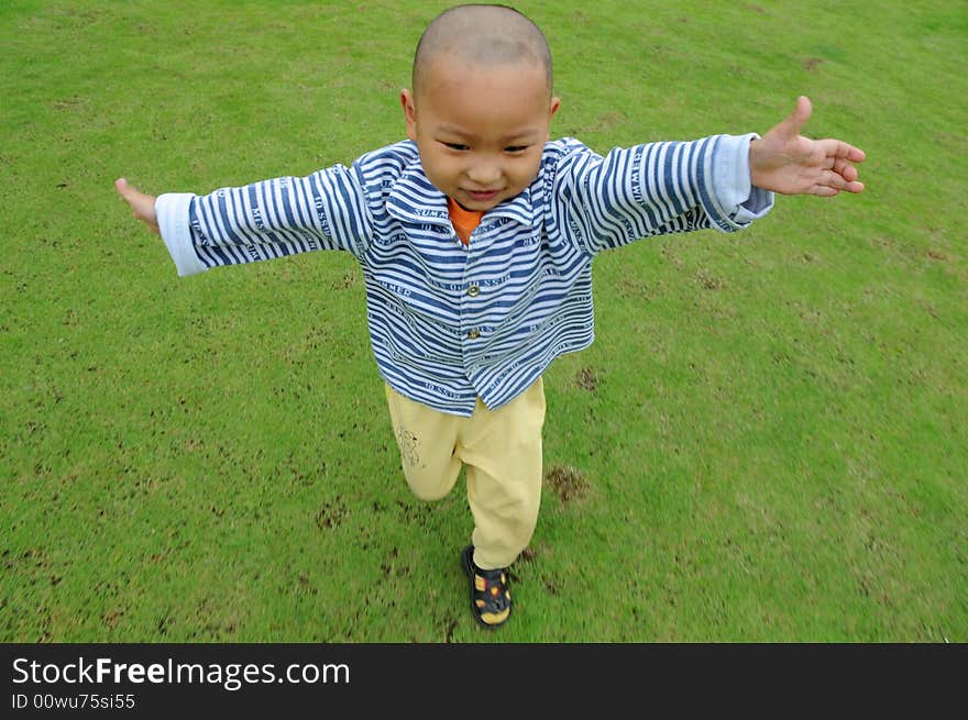 A Chinese little boy run happily on the green meadow. A Chinese little boy run happily on the green meadow.