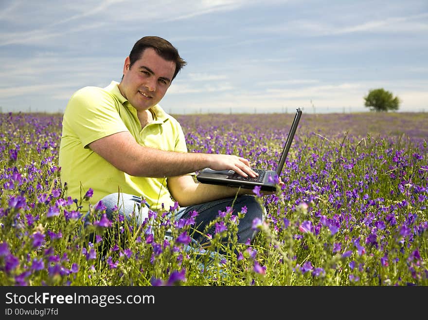 Young man with laptop computer on a flower field