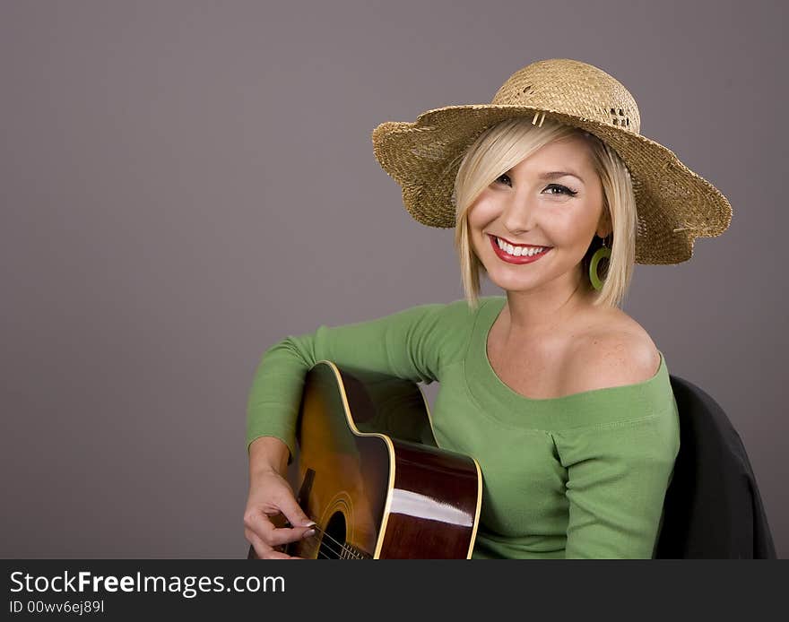 A blonde in a straw hat playing the guitar with a big smile. A blonde in a straw hat playing the guitar with a big smile