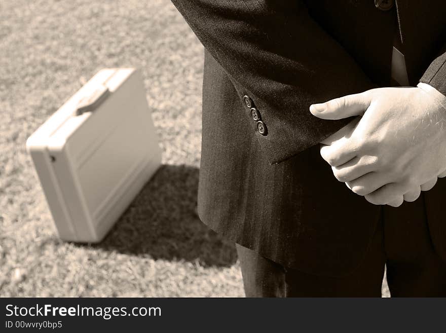 Close up of single businessman standing holding hands with briefcase next to him on grass. Close up of single businessman standing holding hands with briefcase next to him on grass