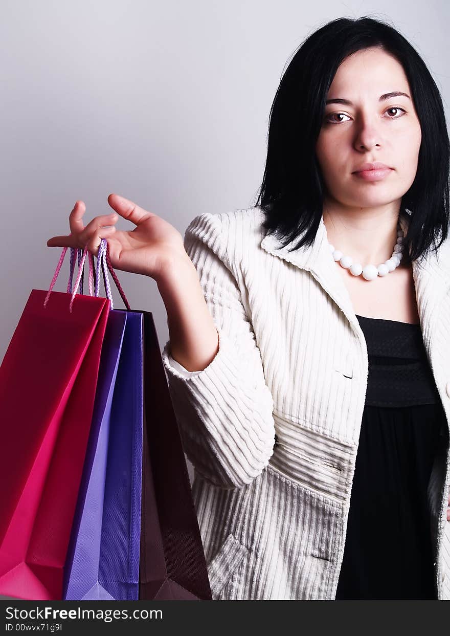 A high-key portrait about a pretty trendy lady with black hair who is holding some shopping bags and she has an attractive look. She is wearing a white coat, a black dress and a white necklace. A high-key portrait about a pretty trendy lady with black hair who is holding some shopping bags and she has an attractive look. She is wearing a white coat, a black dress and a white necklace.