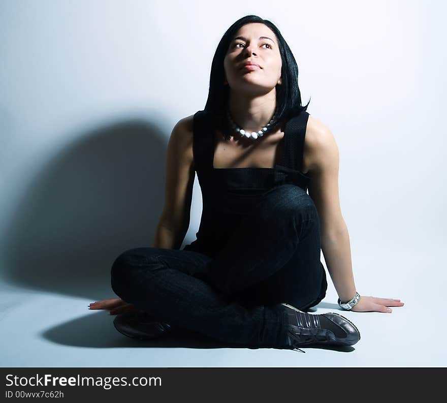 A portrait about an attractive trendy girl with black hair who is sitting, she is spreading her arms on ground, she is looking up and she is admiring something. She is wearing a black dress, blue jeans and a white necklace. A portrait about an attractive trendy girl with black hair who is sitting, she is spreading her arms on ground, she is looking up and she is admiring something. She is wearing a black dress, blue jeans and a white necklace.