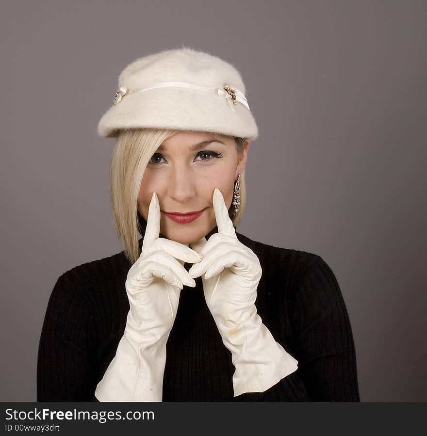 A blonde in black turtleneck and white fur hat with white gloves holding her smile with two fingers. A blonde in black turtleneck and white fur hat with white gloves holding her smile with two fingers