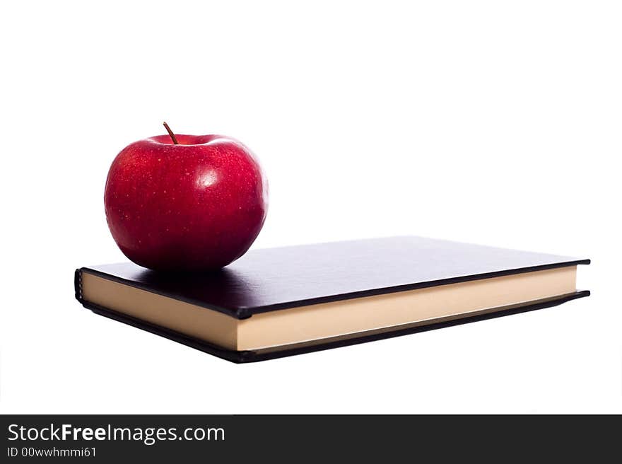 A black school book and a red apple on a white background with copy space. A black school book and a red apple on a white background with copy space