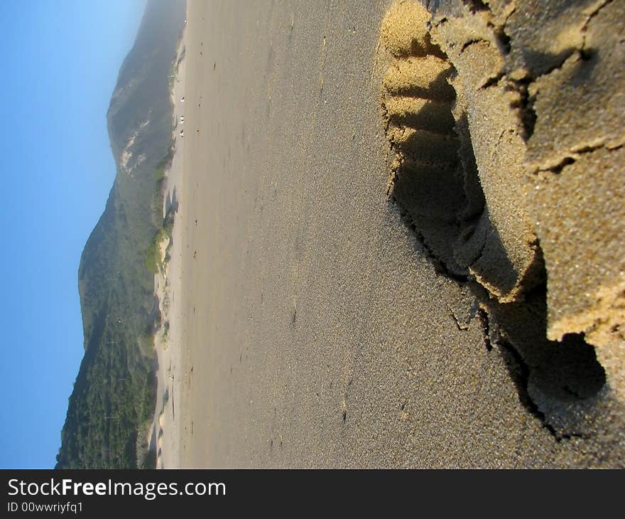 A footprint in the sand at the beach with mountains in the back-round