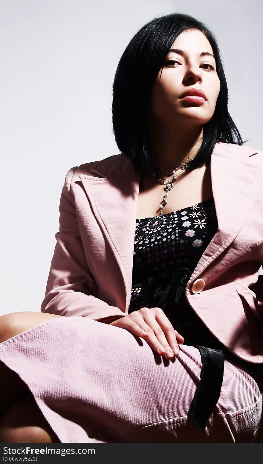 A portrait about an attractive trendy lady with black hair who is sitting on a chair, she is looking ahead and she has a glamorous look. She is wearing a nice dress, a pink skirt, a necklace and a pink stylish coat. A portrait about an attractive trendy lady with black hair who is sitting on a chair, she is looking ahead and she has a glamorous look. She is wearing a nice dress, a pink skirt, a necklace and a pink stylish coat.