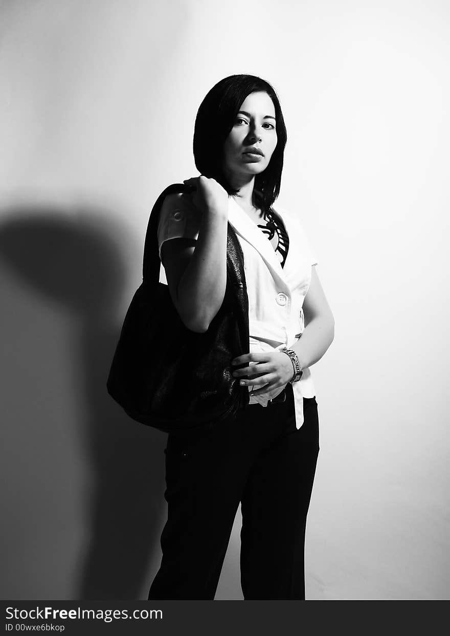 A black and white high-key portrait about a pretty trendy lady with black hair who is looking ahead and she has an attractive look. She is wearing black pants, a white coat and a stylish handbag. A black and white high-key portrait about a pretty trendy lady with black hair who is looking ahead and she has an attractive look. She is wearing black pants, a white coat and a stylish handbag.