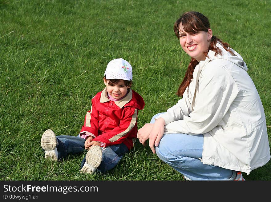 Little girl with her mother in the park sitting on green grass