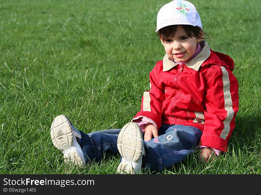 Little girl in the park sitting on green grass