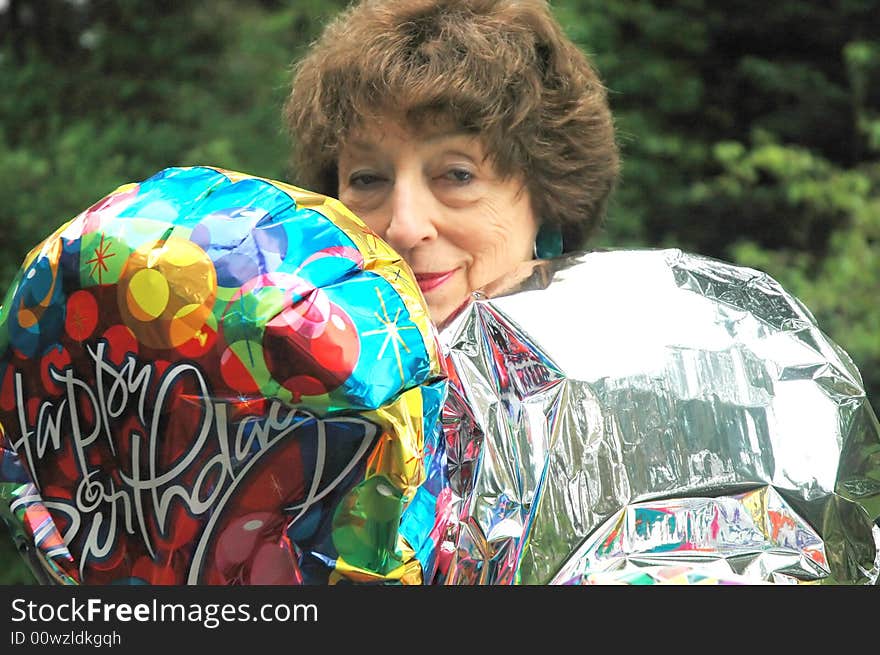 Mature female senior relaxing at home on her outdoor deck with happy birthday balloons.