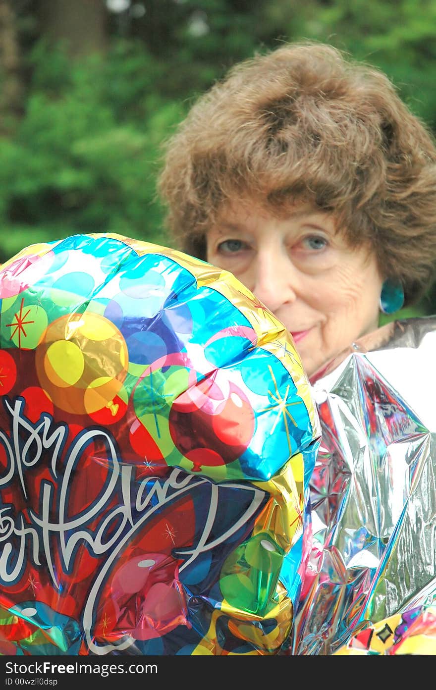 Mature female senior relaxing at home on her outdoor deck with happy birthday balloons.